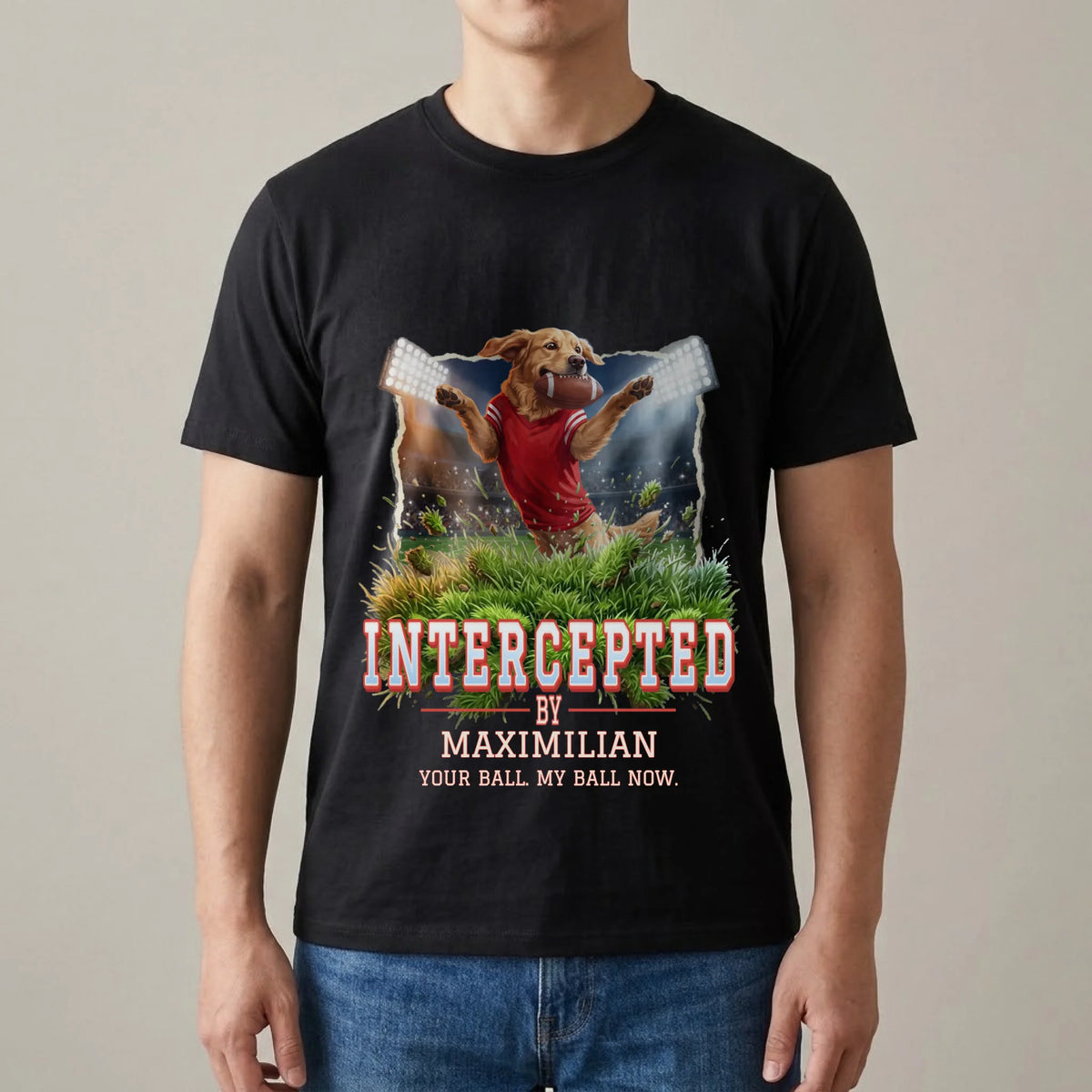 Man wearing a black T-shirt with a personalized print: golden retriever in a red jersey leaping under stadium floodlights with a football in its mouth, "Intercepted by Maximilian" and "Your ball. My ball now."