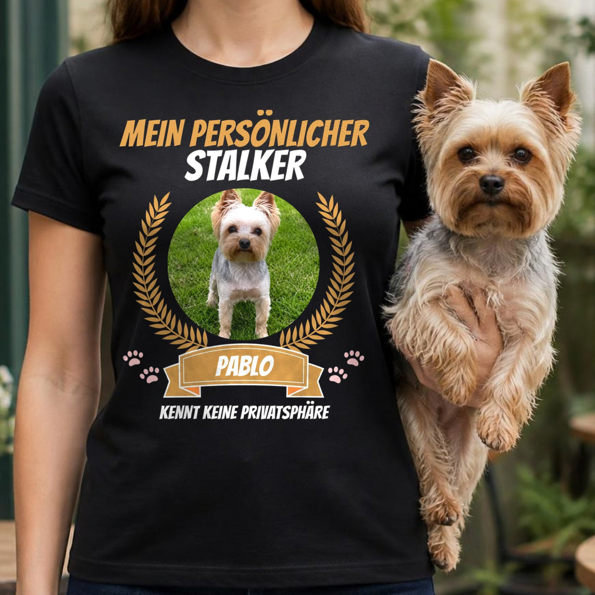 Frau traegt schwarzes T-Shirt Mein persoenlicher Stalker mit Yorkshire Terrier auf dem Arm auf Cafe-Terrasse