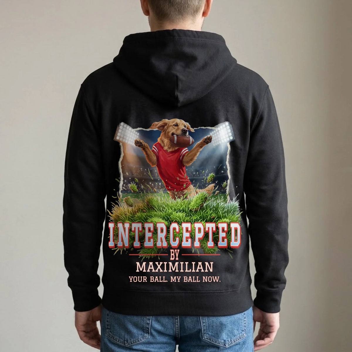 Man wearing a black hoodie, back print: golden retriever in a red jersey catching a football under stadium floodlights, "Intercepted by Maximilian" and "Your ball. My ball now."